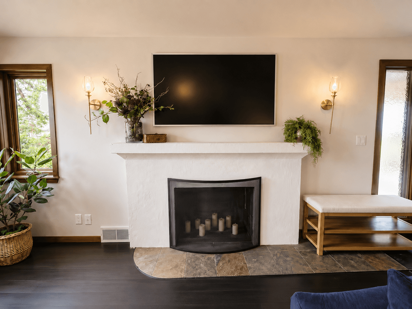 A white plaster fireplace with a slate tile hearth, flanked by brass sconces in a styled living room.