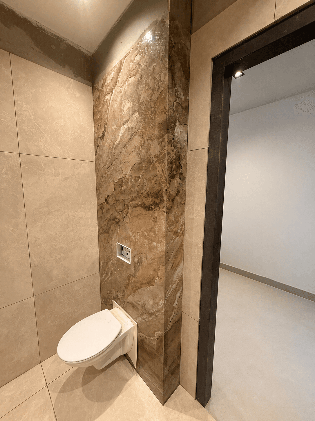 A dramatic book-matched brown marble accent wall wrapping a corner beside large-format beige tile.